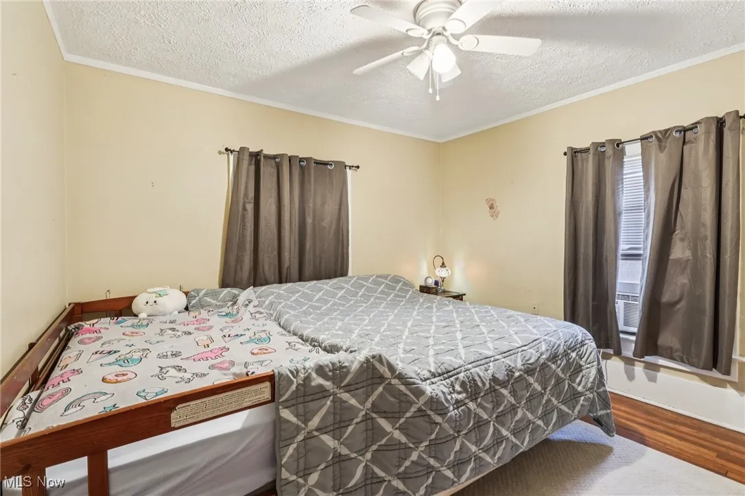 Bedroom with wood finished floors, a textured ceiling, ornamental molding, and ceiling fan