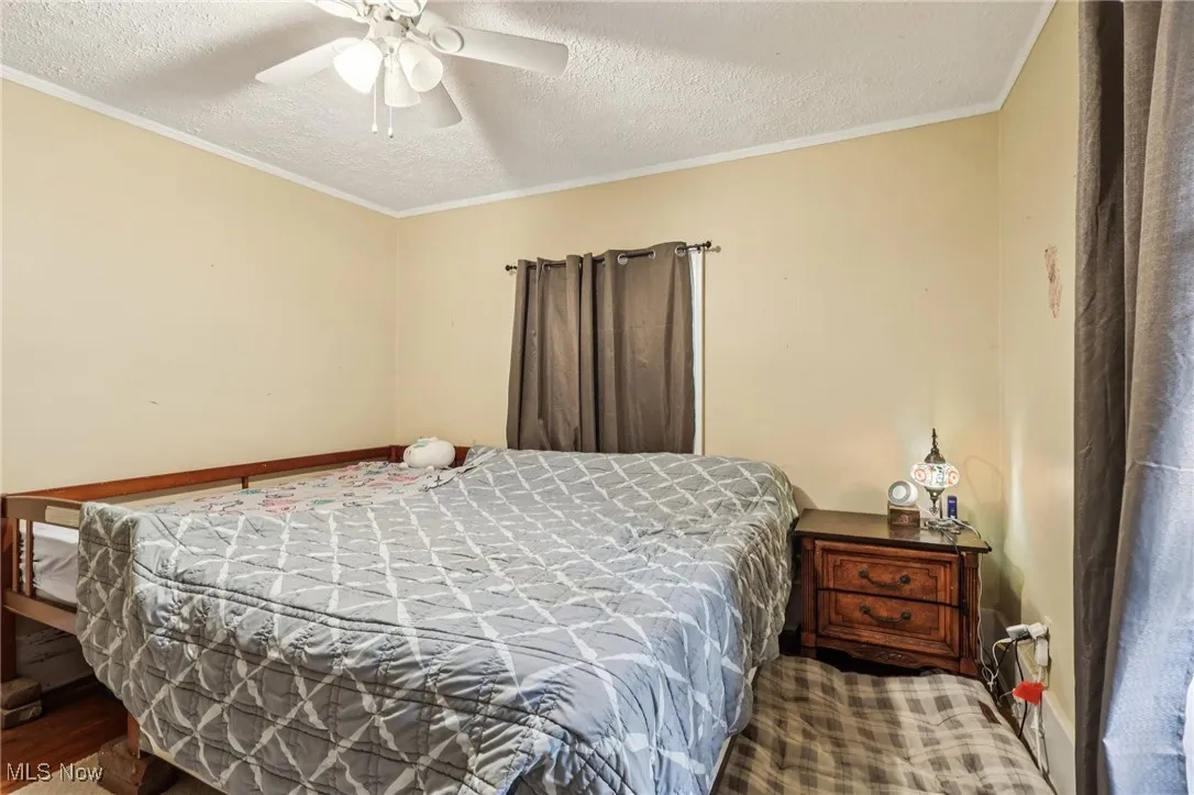 Bedroom with a textured ceiling, ornamental molding, and a ceiling fan