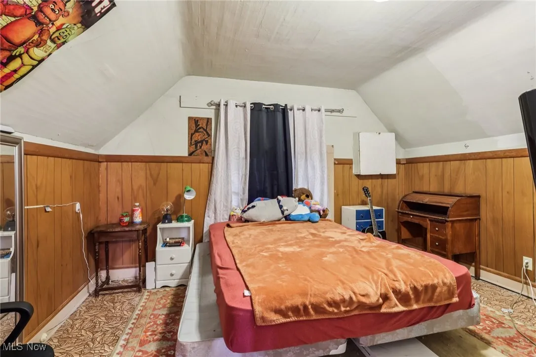 Bedroom featuring wooden walls and lofted ceiling