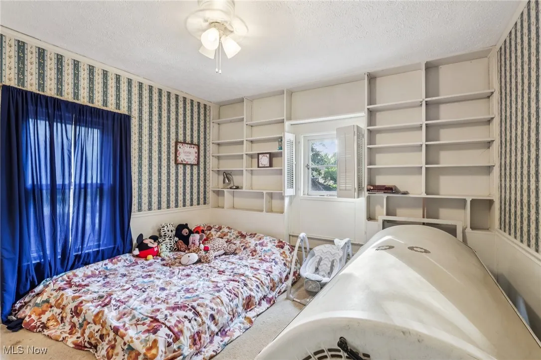 Carpeted bedroom with wallpapered walls, a textured ceiling, and wainscoting