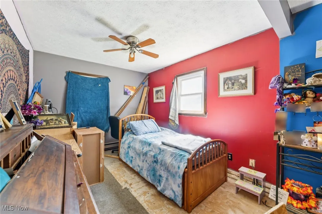 Carpeted bedroom with a textured ceiling, a ceiling fan, and a baseboard heating unit
