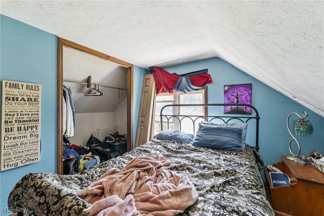 Bedroom with lofted ceiling, a textured ceiling, and a closet