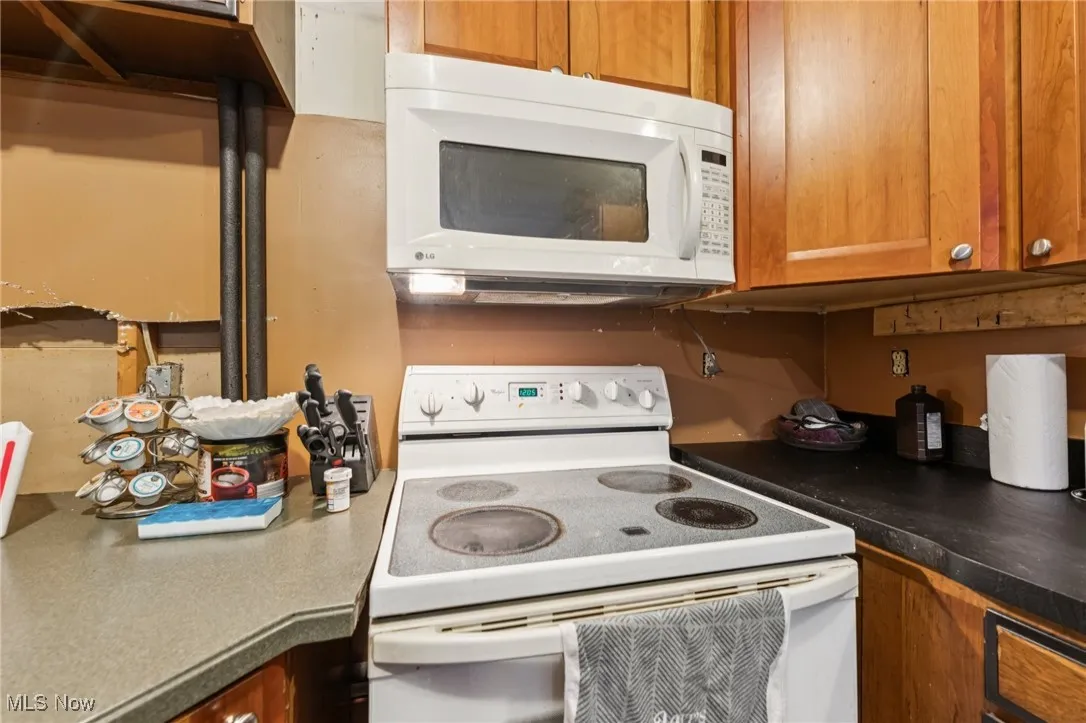 Kitchen featuring white appliances, brown cabinetry, and dark countertops