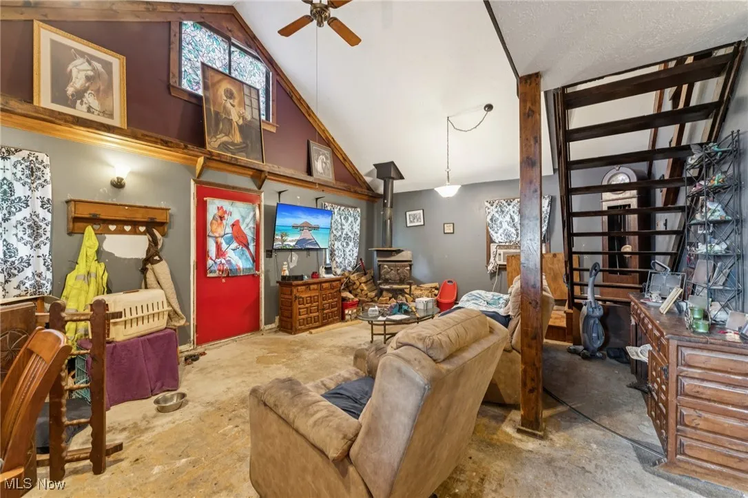 Living room with a wood stove, a ceiling fan, and high vaulted ceiling