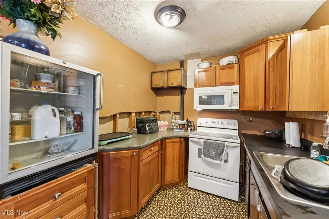 Kitchen featuring white appliances, a textured ceiling, brown cabinetry, dark countertops, and a peninsula