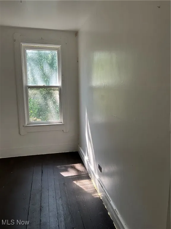 Spare room featuring baseboards and dark wood-style flooring