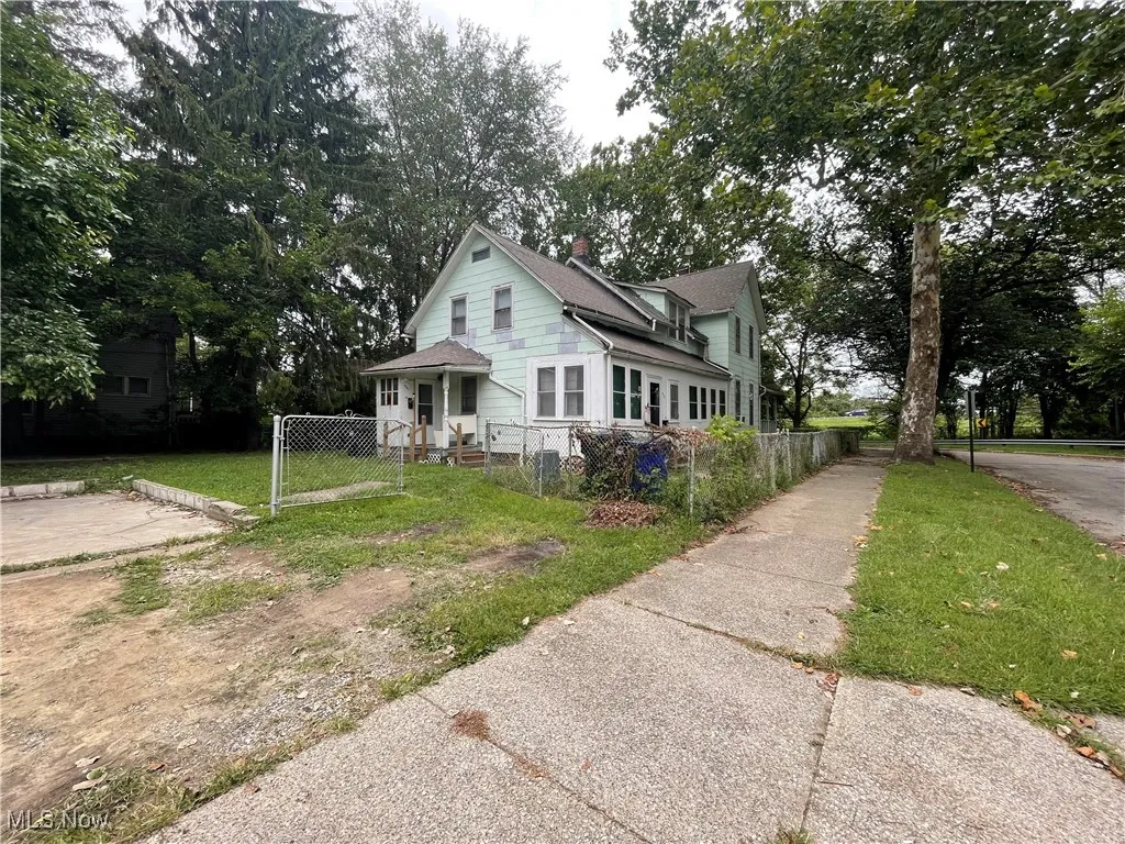 View of front facade with a porch, a chimney, view of scattered trees, and a fenced front yard