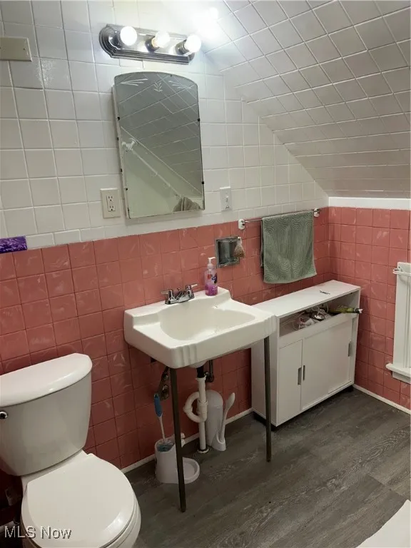 Half bathroom with tile walls, dark wood finished floors, and vaulted ceiling