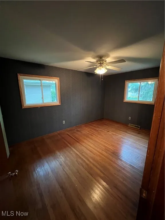 Empty room with hardwood / wood-style floors, healthy amount of natural light, and ceiling fan