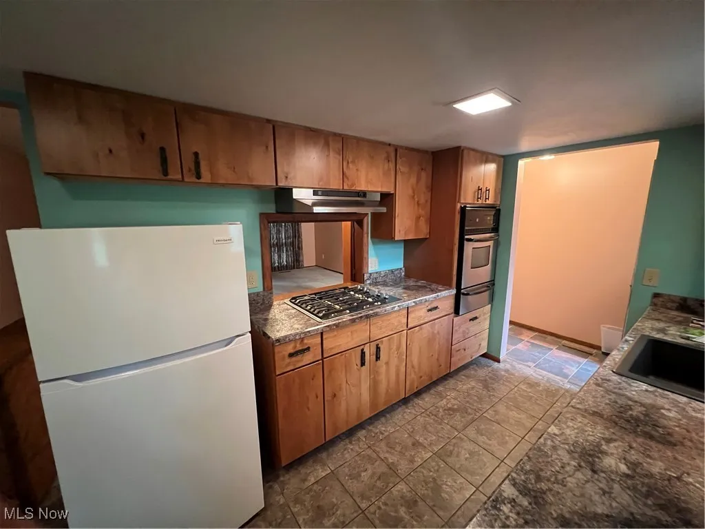 Kitchen with fridge, dark stone countertops, oven, cooktop, and a warming drawer