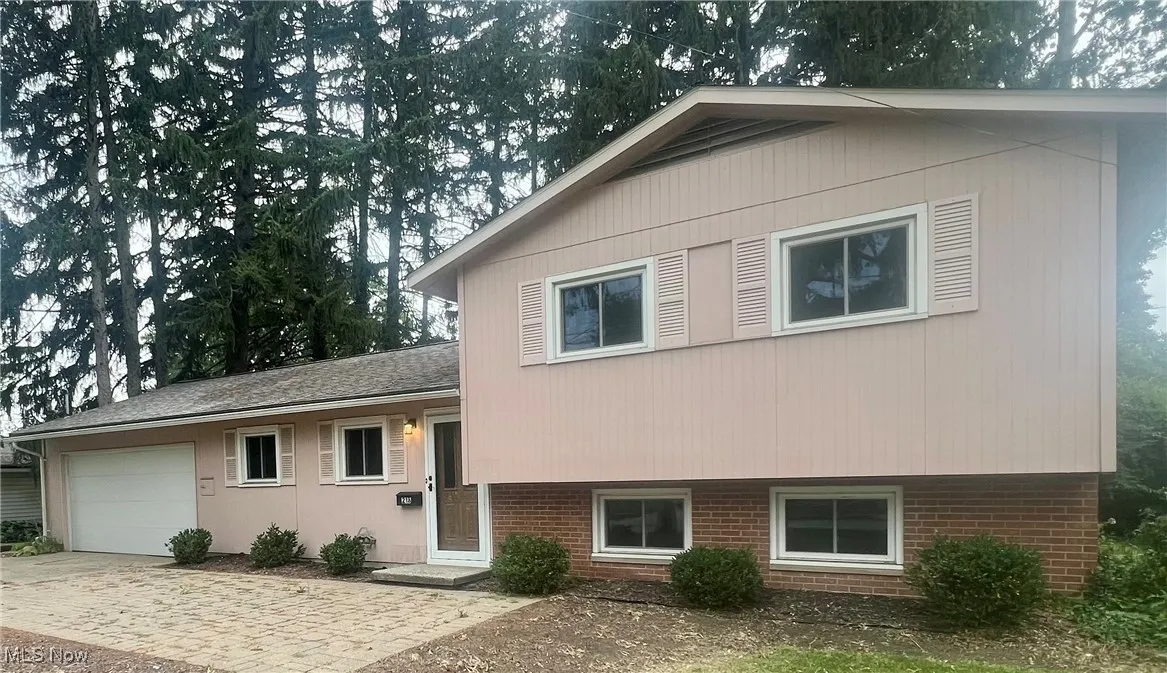 Split level home with brick siding, an attached garage, and driveway