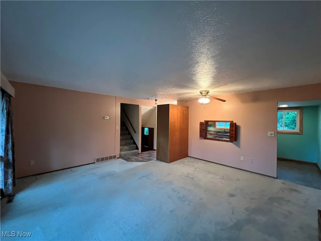 Unfurnished living room featuring a textured ceiling, ceiling fan, and stairway