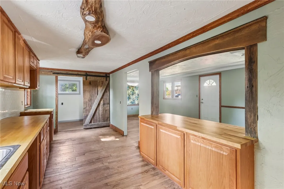 Kitchen featuring a barn door, wooden counters, light wood finished floors, a textured ceiling, and brown cabinetry