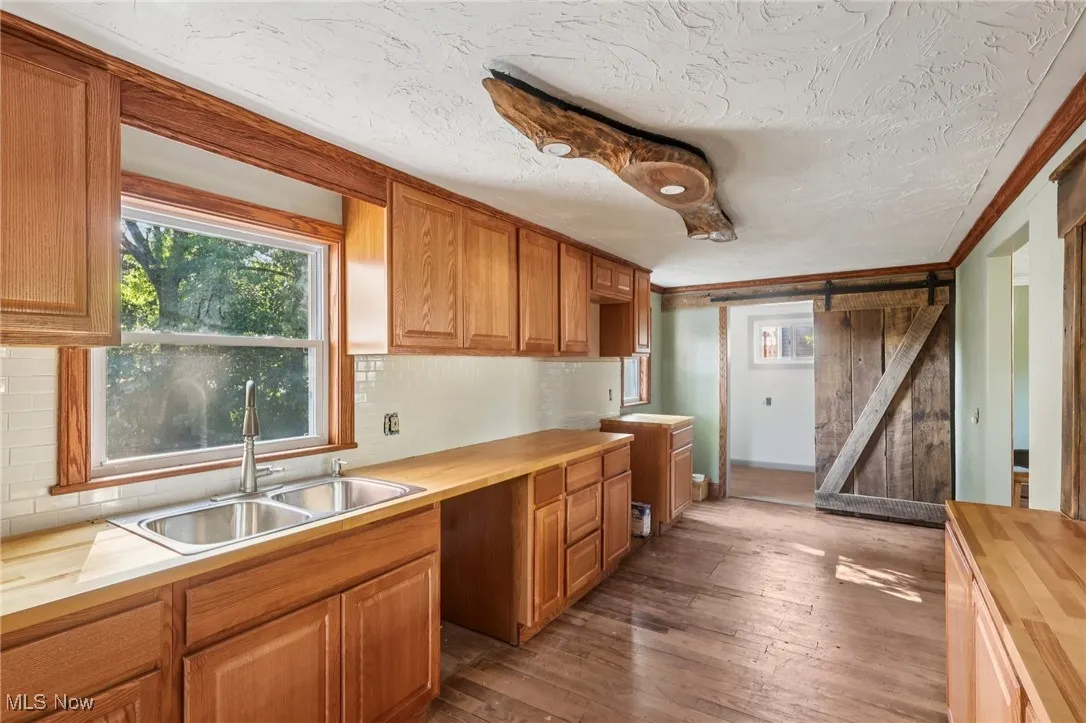 Kitchen featuring wooden counters, a barn door, dark wood-style flooring, a textured ceiling, and brown cabinetry