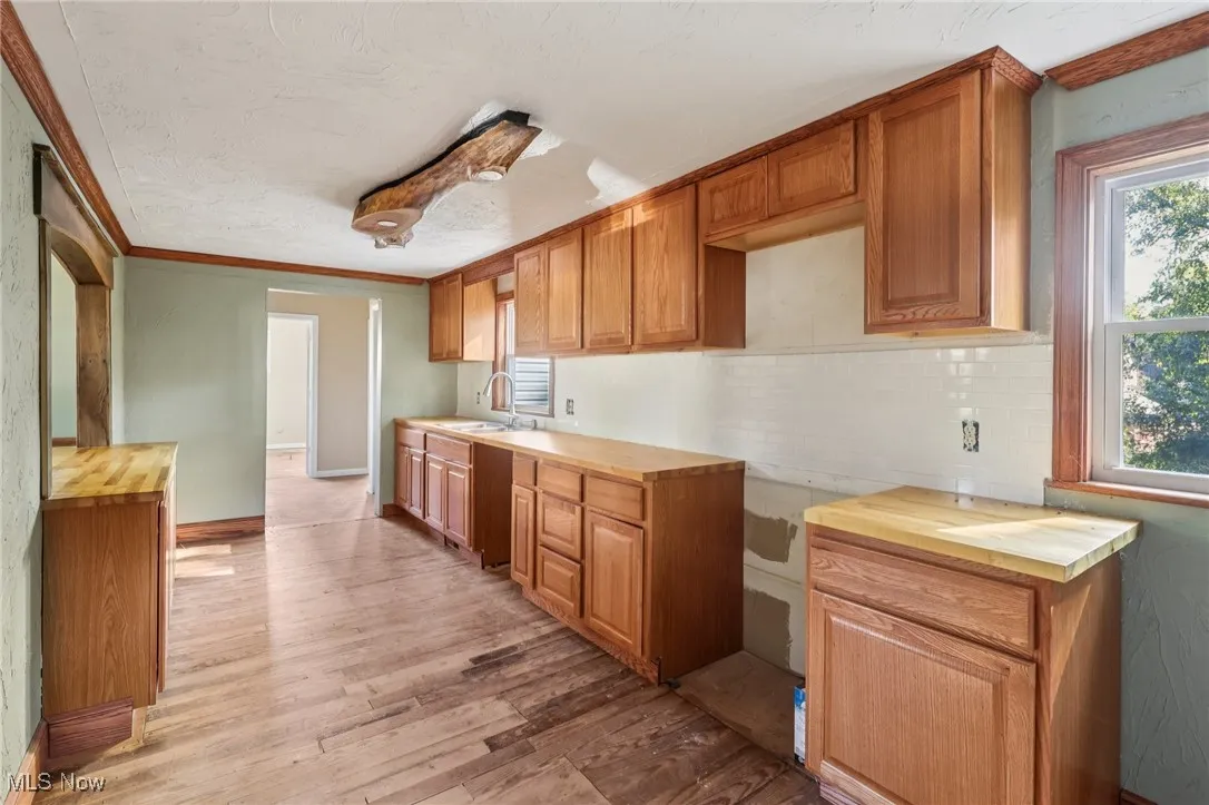 Kitchen featuring wood counters, crown molding, light wood-style floors, healthy amount of natural light, and backsplash