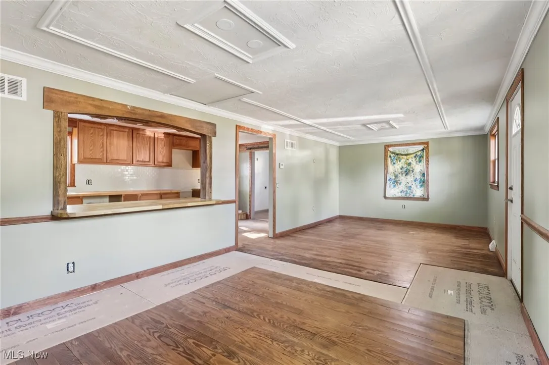 Unfurnished living room featuring wood finished floors, ornamental molding, and a textured ceiling