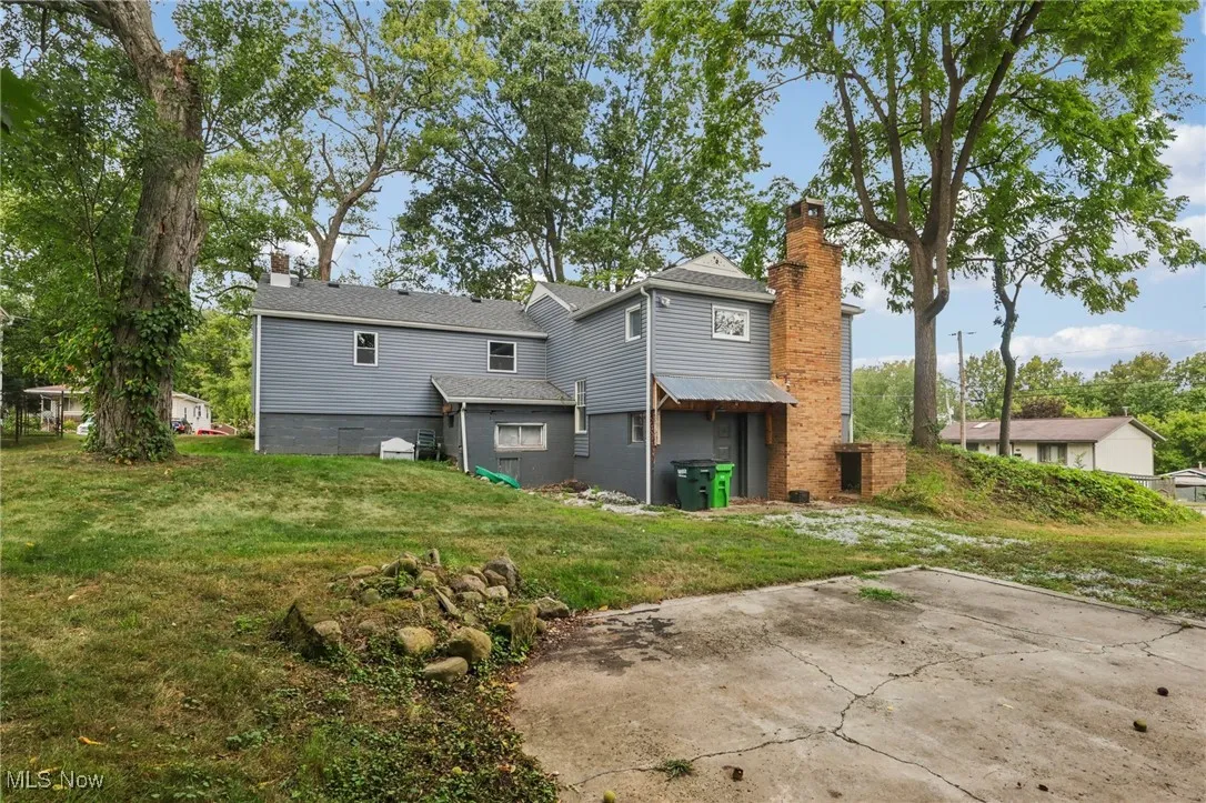 Rear view of house with a chimney, a yard, and a shingled roof