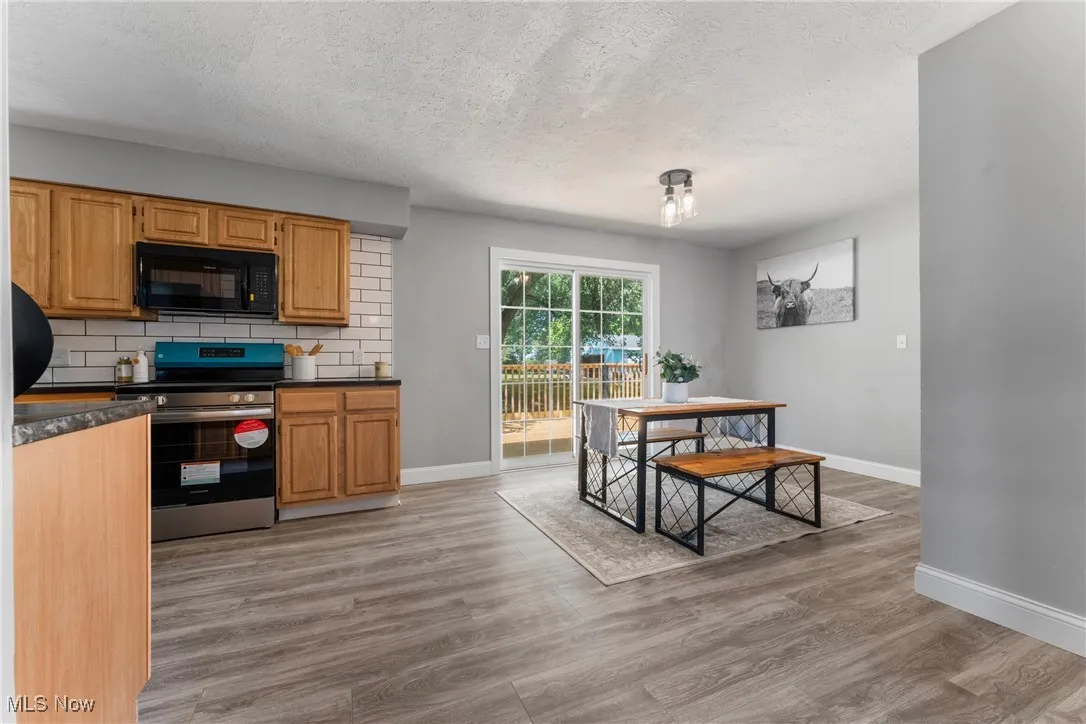 Kitchen featuring backsplash, stainless steel range with electric stovetop, black microwave, light wood finished floors, and a textured ceiling