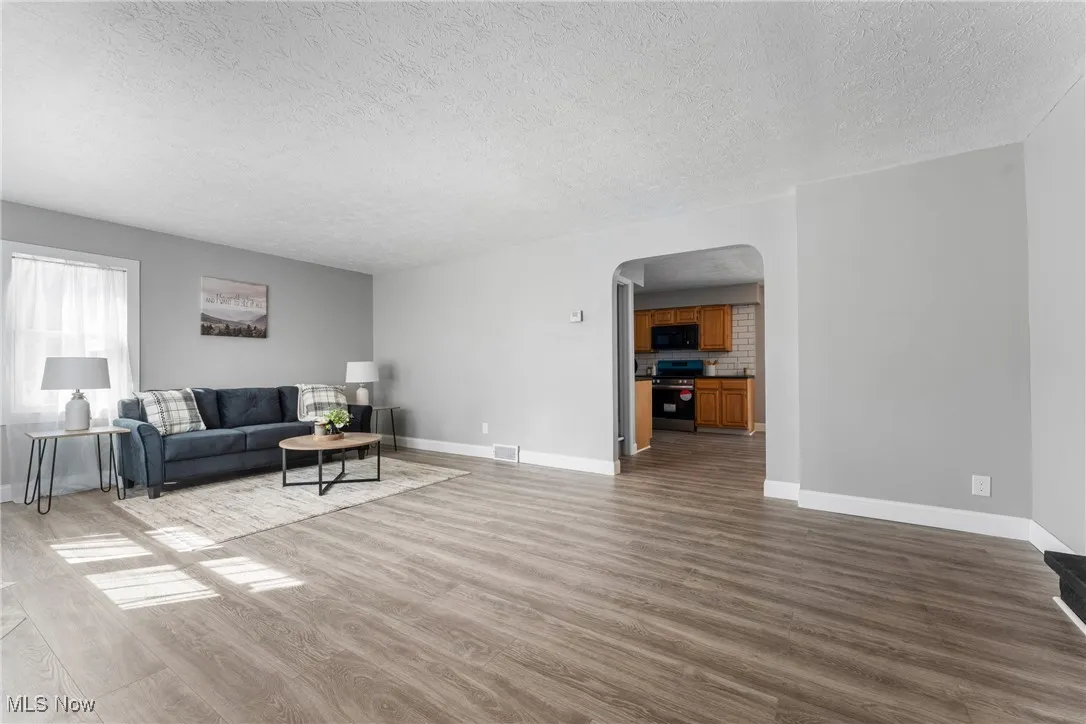 Living room with light wood-style flooring, arched walkways, and a textured ceiling