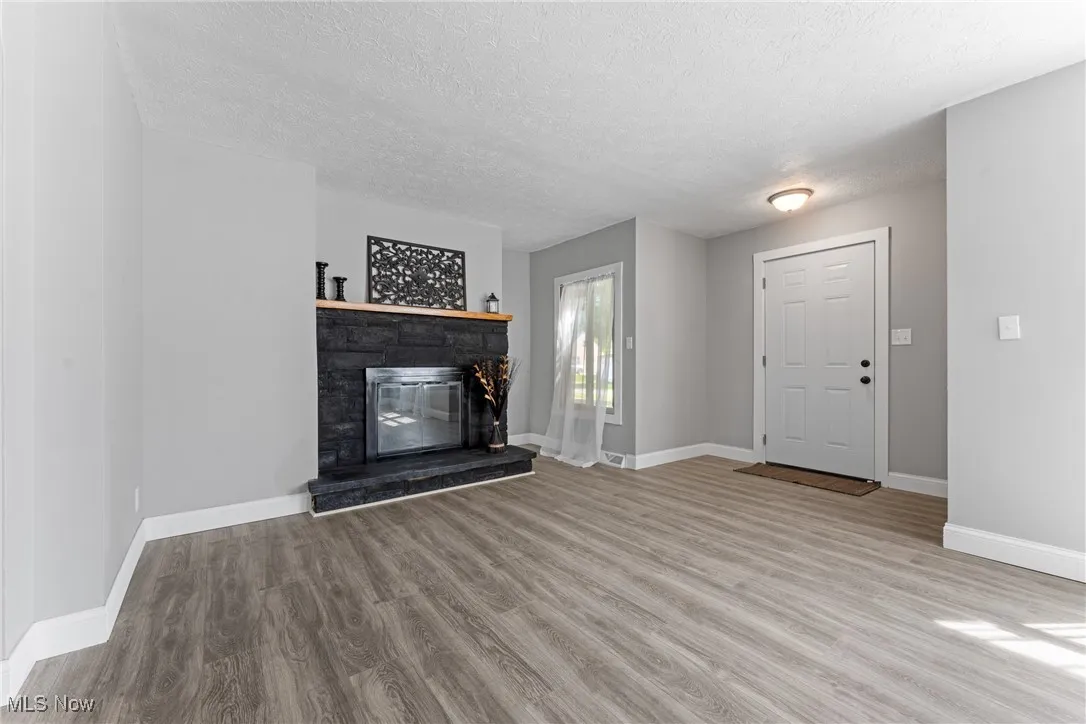 Unfurnished living room with a stone fireplace, light wood-style flooring, and a textured ceiling