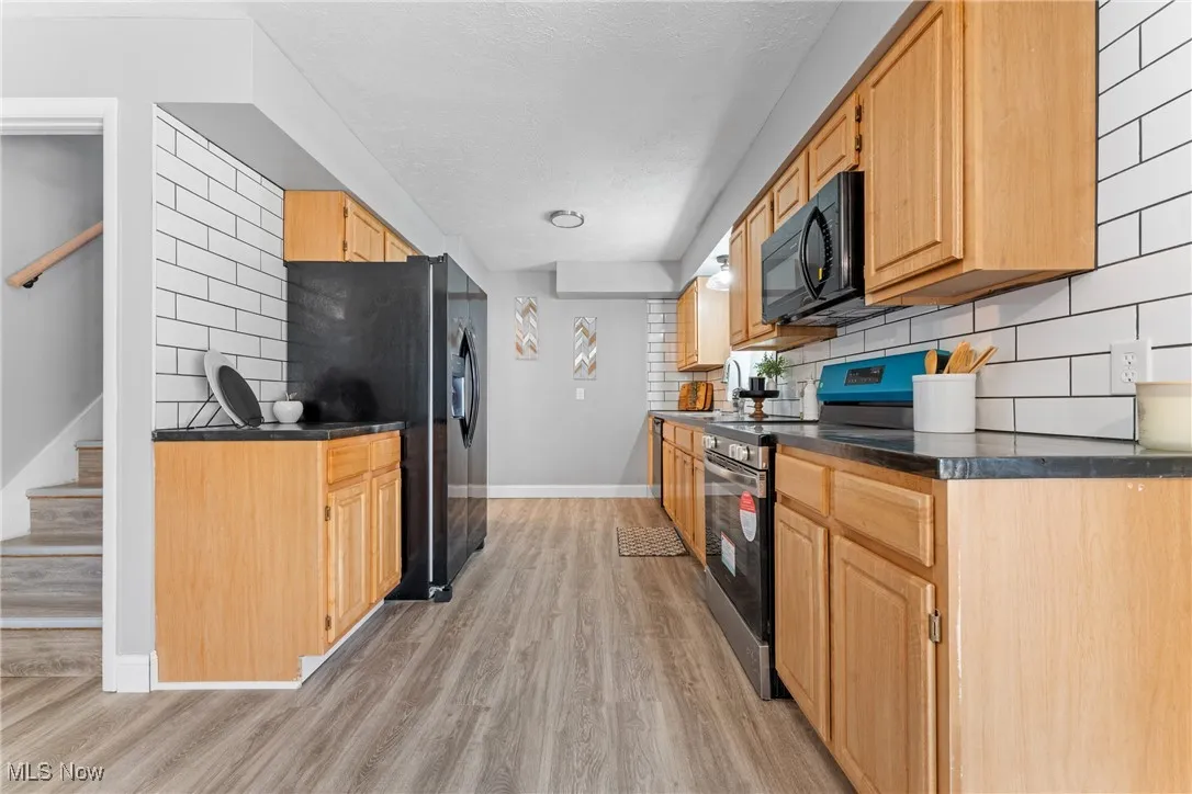 Kitchen with black appliances, light wood-type flooring, decorative backsplash, and light brown cabinetry