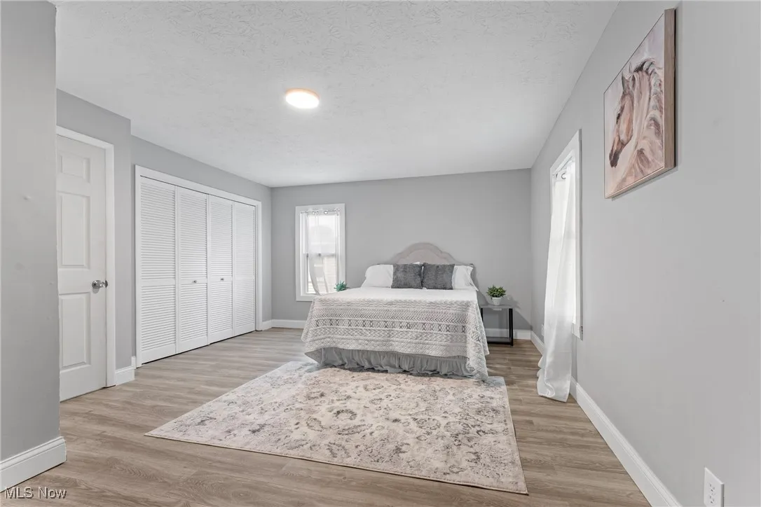 Bedroom with light wood-type flooring, a textured ceiling, multiple windows, and a closet