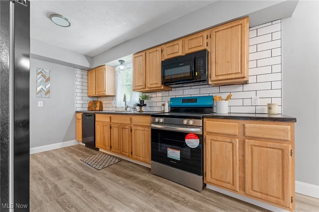 Kitchen featuring decorative backsplash, black appliances, light wood finished floors, dark countertops, and a textured ceiling