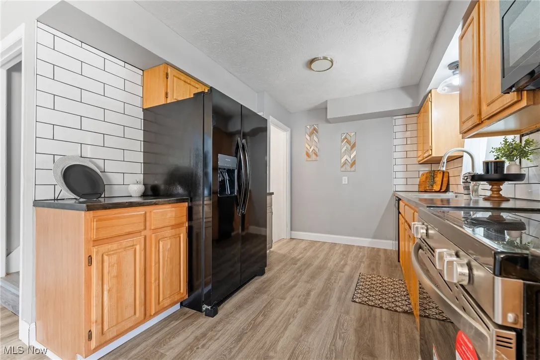 Kitchen featuring tasteful backsplash, black appliances, light wood-type flooring, a textured ceiling, and light brown cabinets