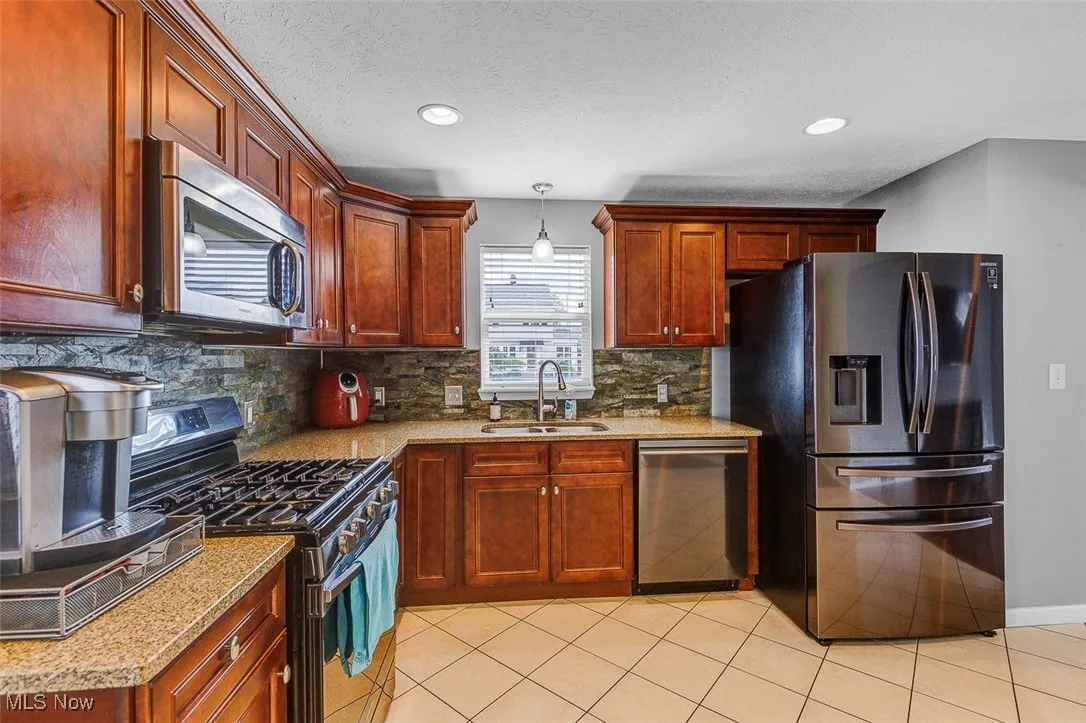 Kitchen featuring stainless steel appliances, light tile patterned flooring, decorative light fixtures, a textured ceiling, and light stone countertops