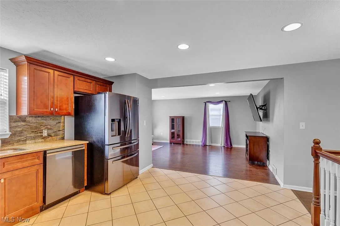 Kitchen featuring light tile patterned flooring, brown cabinetry, dishwasher, light stone counters, and recessed lighting