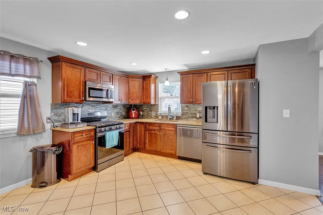 Kitchen with stainless steel appliances, brown cabinets, tasteful backsplash, light tile patterned floors, and recessed lighting