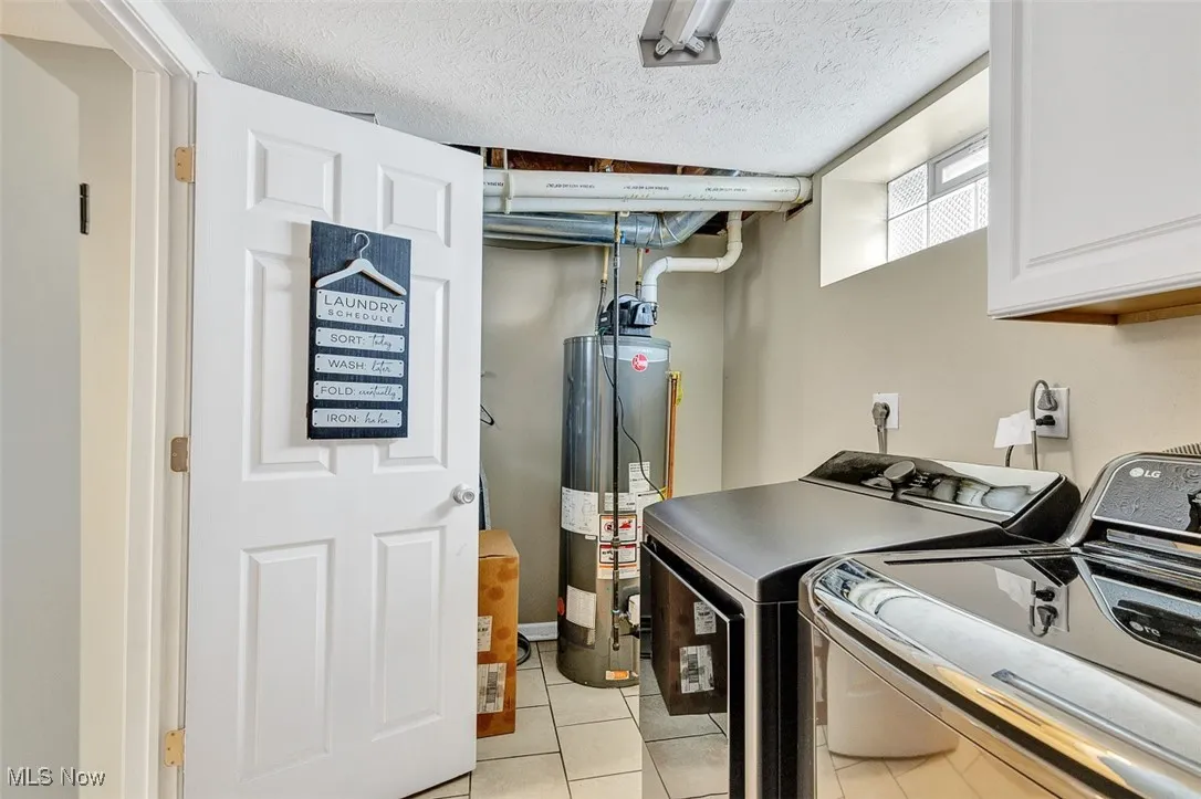 Laundry room with light tile patterned floors, gas water heater, a textured ceiling, cabinet space, and washing machine and dryer