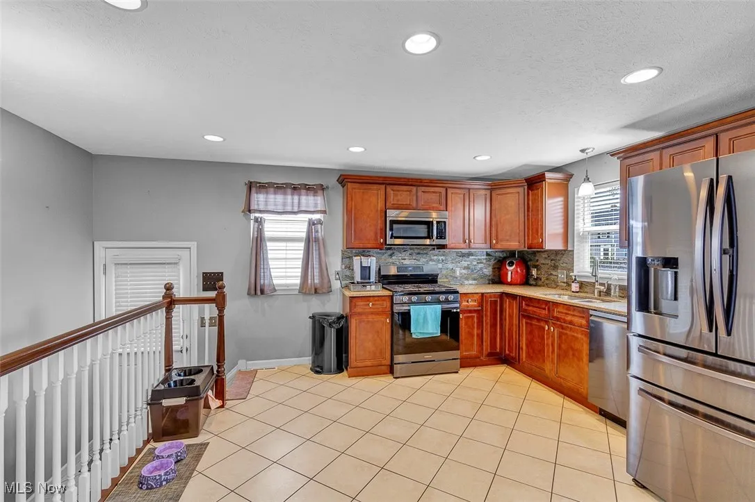 Kitchen with appliances with stainless steel finishes, brown cabinets, tasteful backsplash, recessed lighting, and light tile patterned floors