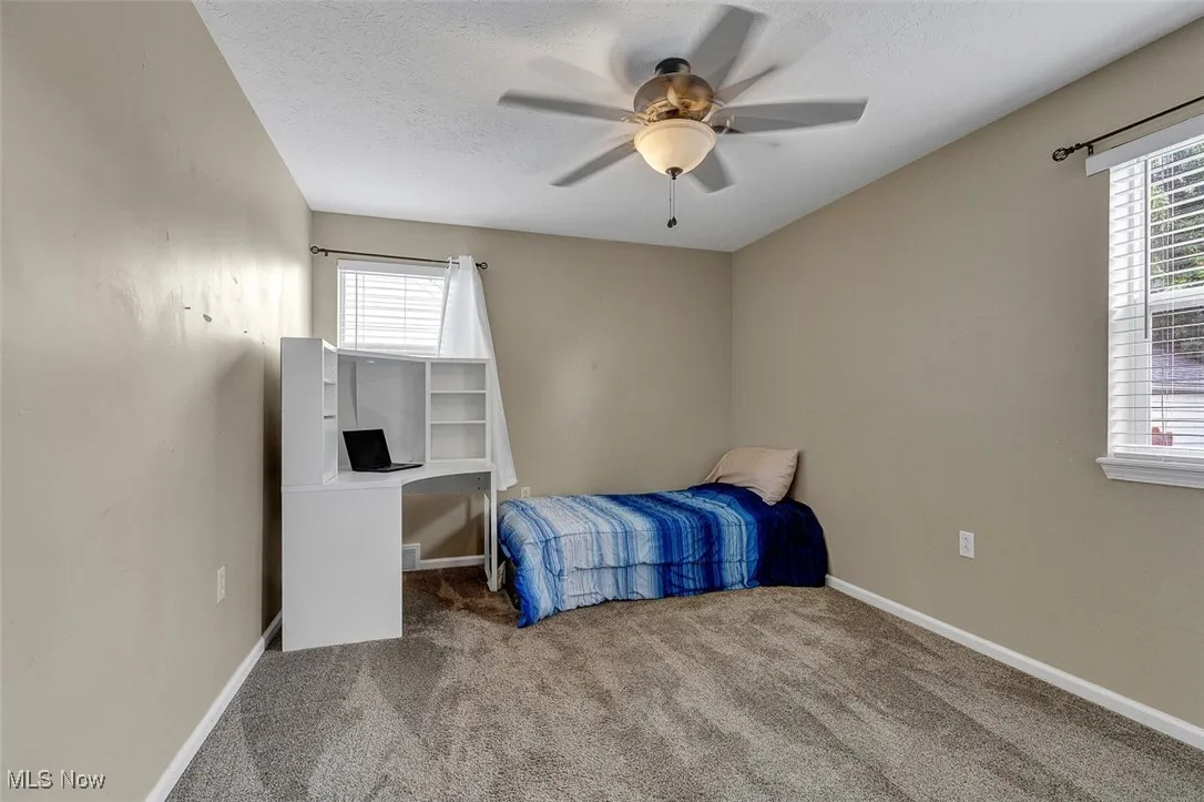 Carpeted bedroom featuring ceiling fan, multiple windows, and a textured ceiling
