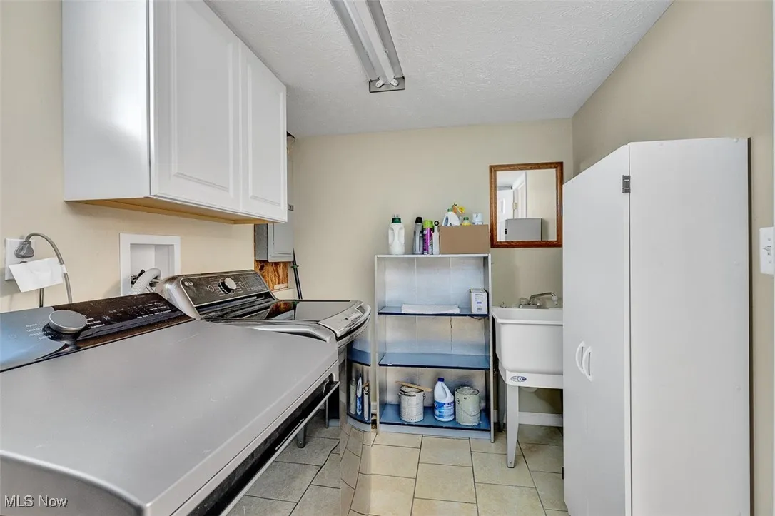 Laundry room featuring light tile patterned floors, cabinet space, a textured ceiling, and washer and clothes dryer
