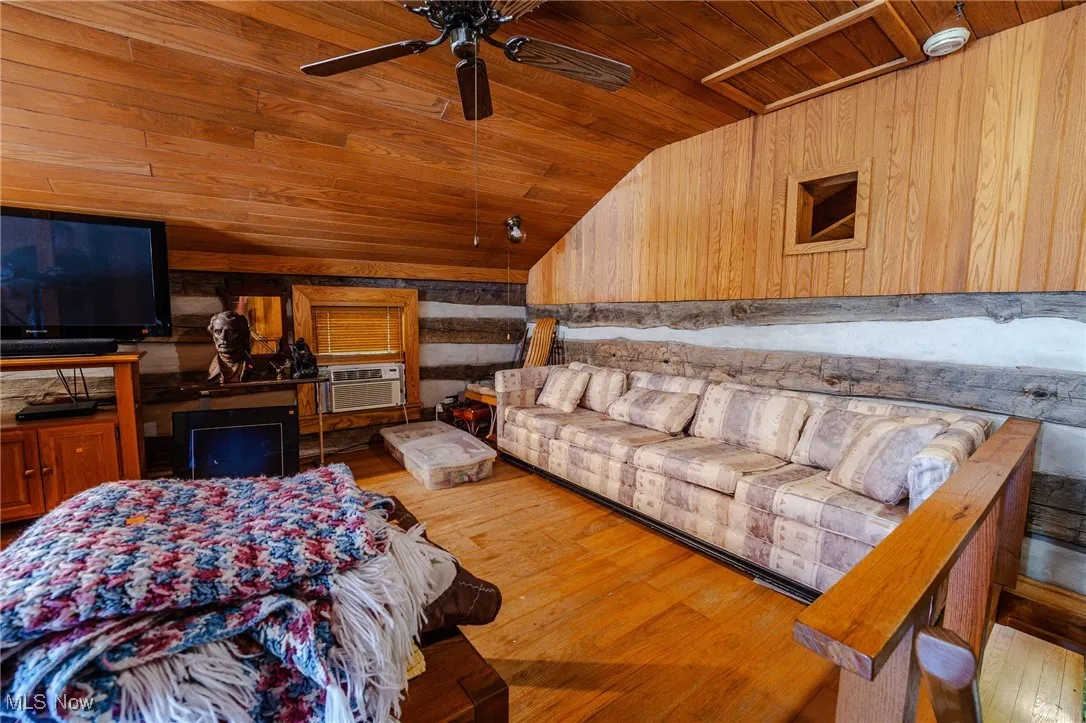 Living room with vaulted ceiling, wooden ceiling, hardwood / wood-style floors, and wooden walls