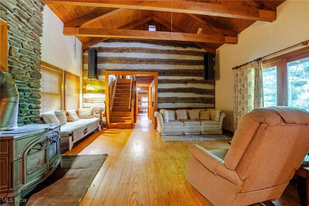 Living room with high vaulted ceiling, a wooden ceiling with exposed beams, a wood stove, hardwood / wood-style flooring, and stairway