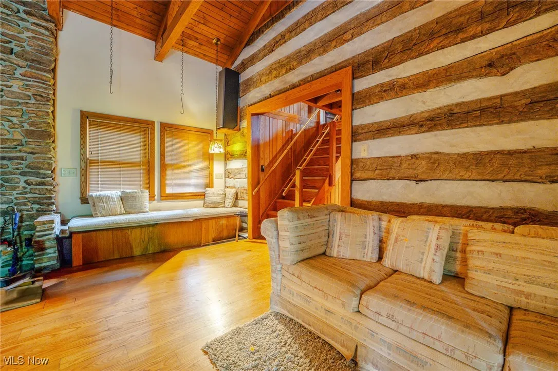Living area featuring a wood ceiling with exposed beams, light wood finished floors, high vaulted ceiling, and stairway