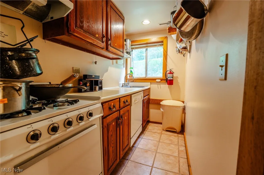 Kitchen featuring light countertops, white appliances, ventilation hood, brown cabinets, and light tile patterned flooring
