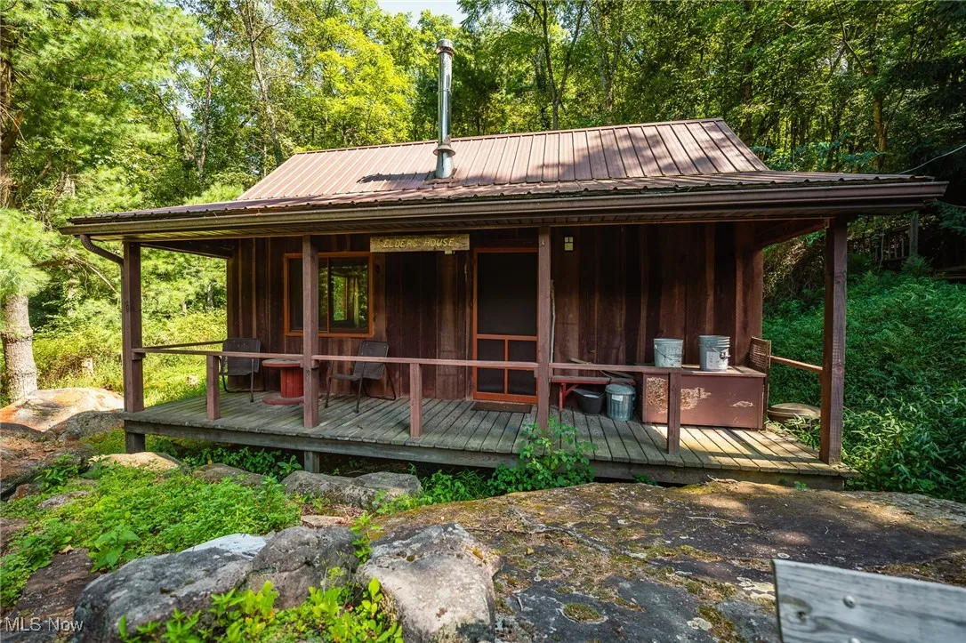 Rear view of property featuring covered porch, a metal roof, board and batten siding, and a forest view
