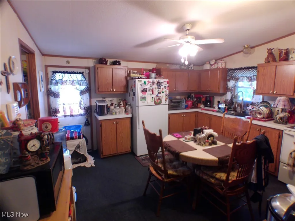 Kitchen with white appliances, light countertops, brown cabinetry, crown molding, and ceiling fan