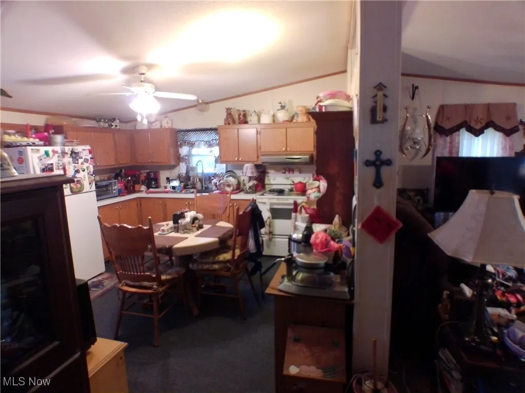 Kitchen featuring white appliances, ornamental molding, light countertops, dark carpet, and under cabinet range hood