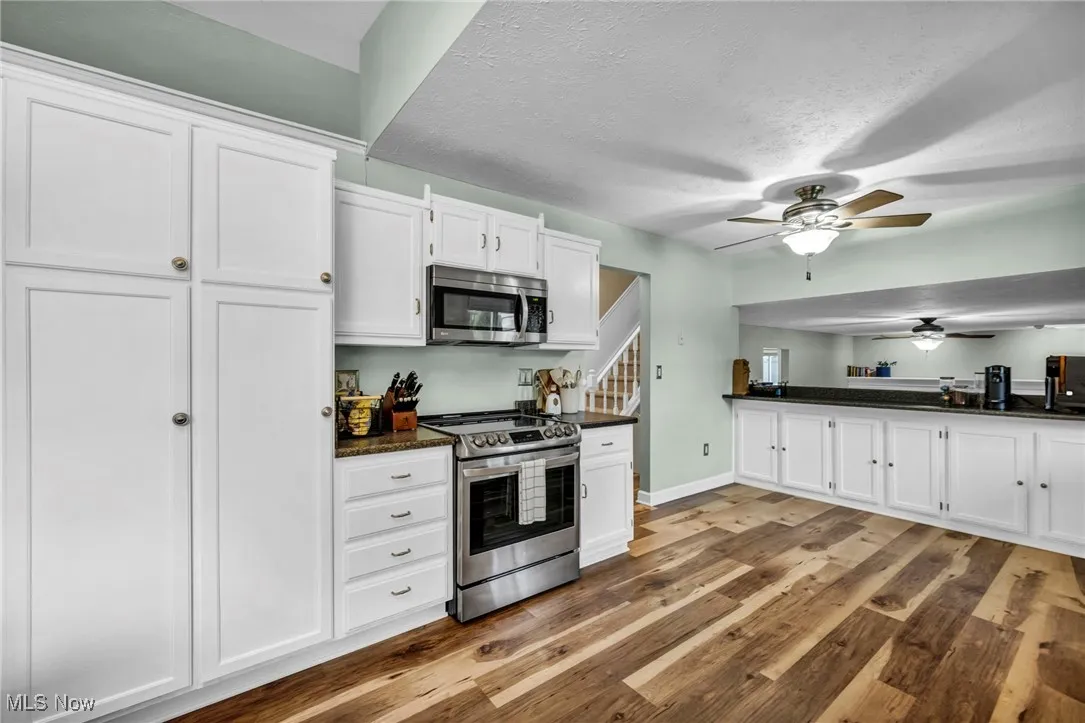 Kitchen featuring white cabinets, stainless steel appliances, a ceiling fan, light wood finished floors, and a textured ceiling