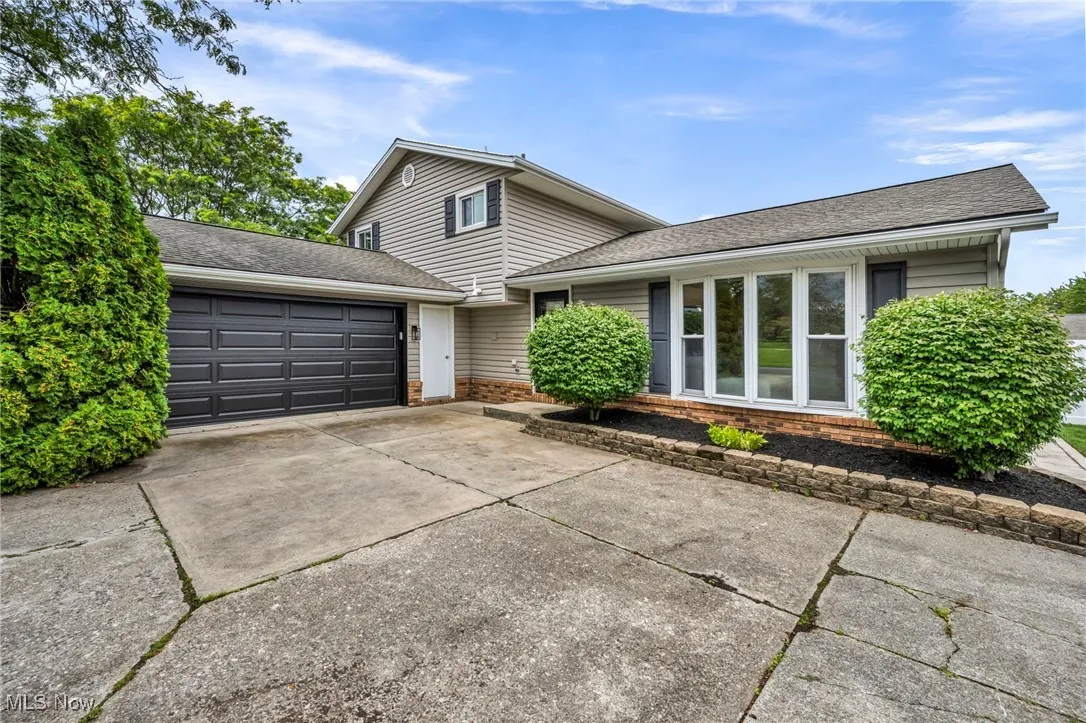 Split level home with roof with shingles, an attached garage, concrete driveway, and brick siding