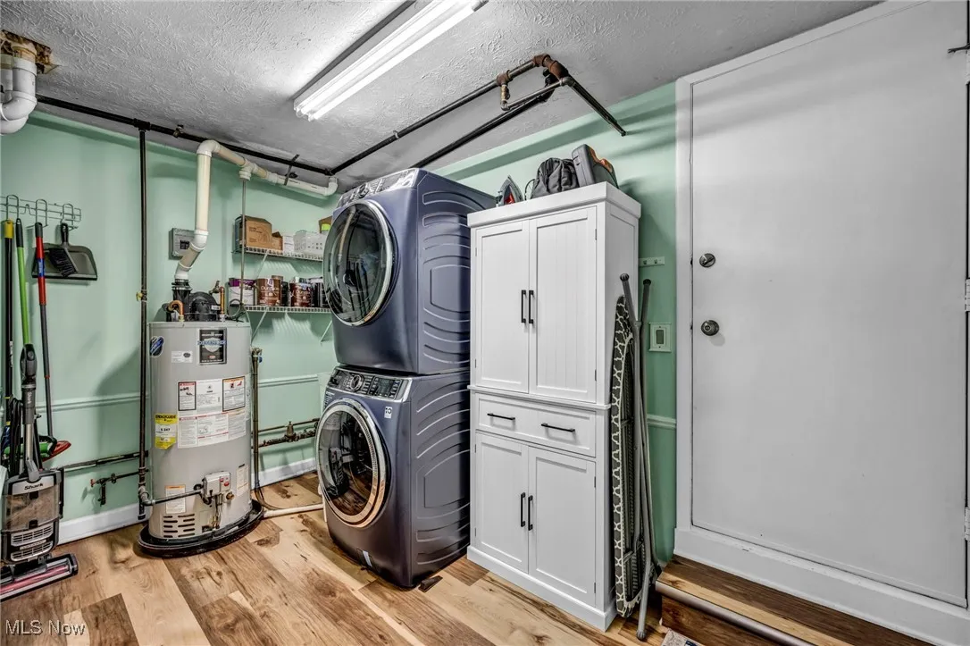 Laundry area featuring stacked washer and clothes dryer, a textured ceiling, light wood finished floors, gas water heater, and cabinet space