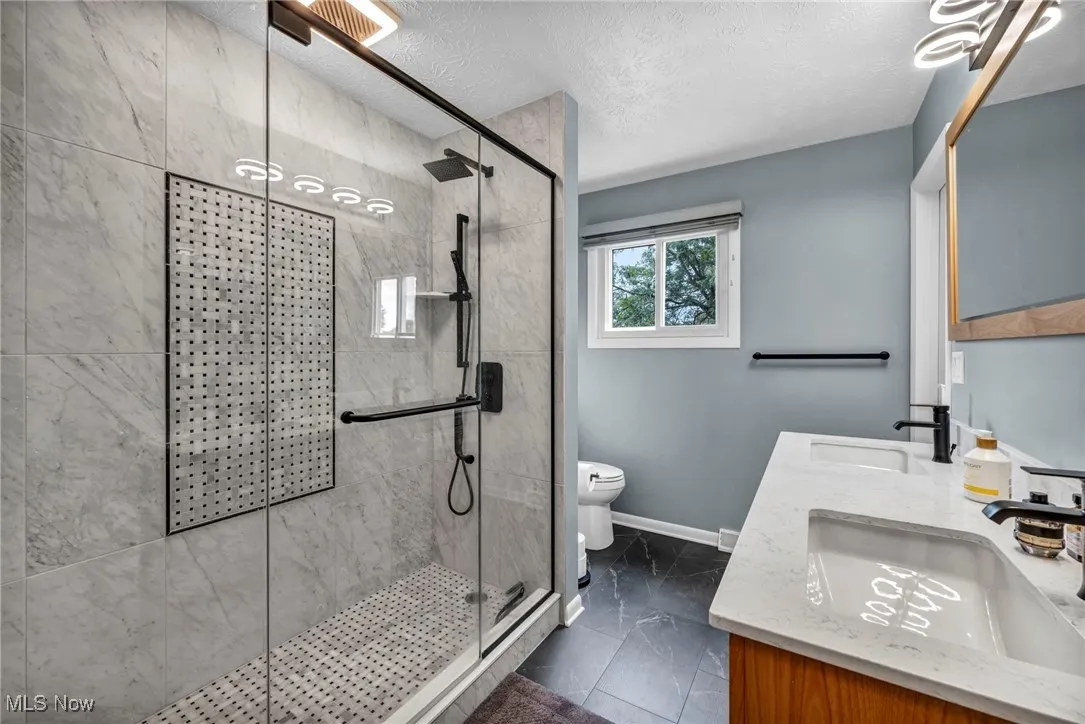 Full bath with a stall shower, double vanity, a textured ceiling, and dark marble finish flooring