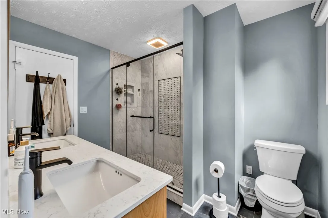 Bathroom featuring a stall shower, double vanity, and a textured ceiling