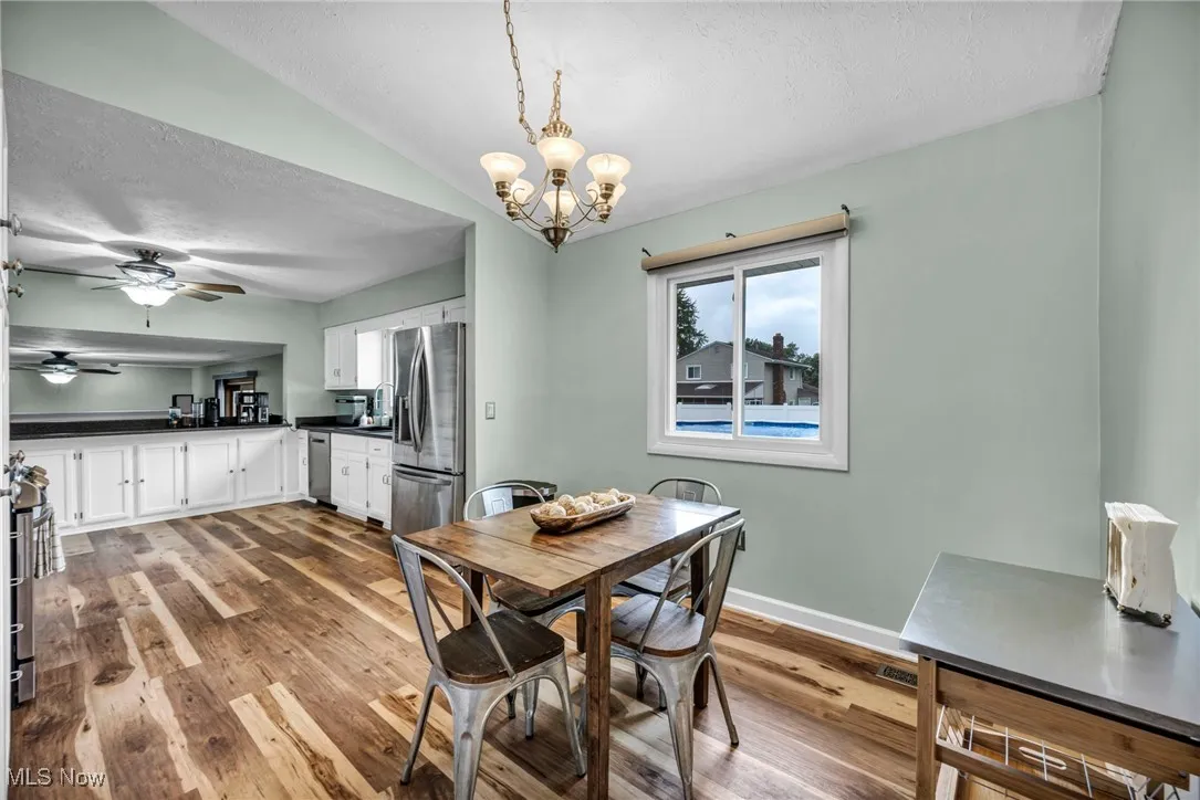 Dining space with a textured ceiling, light wood-style flooring, a ceiling fan, a chandelier, and lofted ceiling