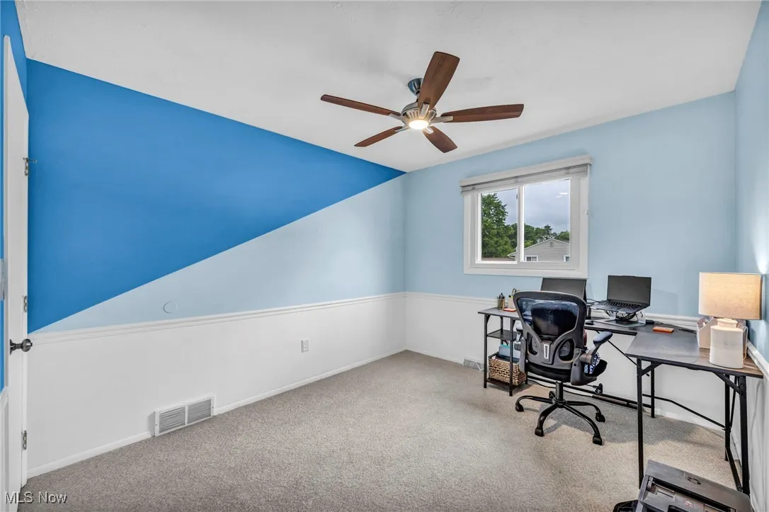 Carpeted home office featuring ceiling fan and baseboards