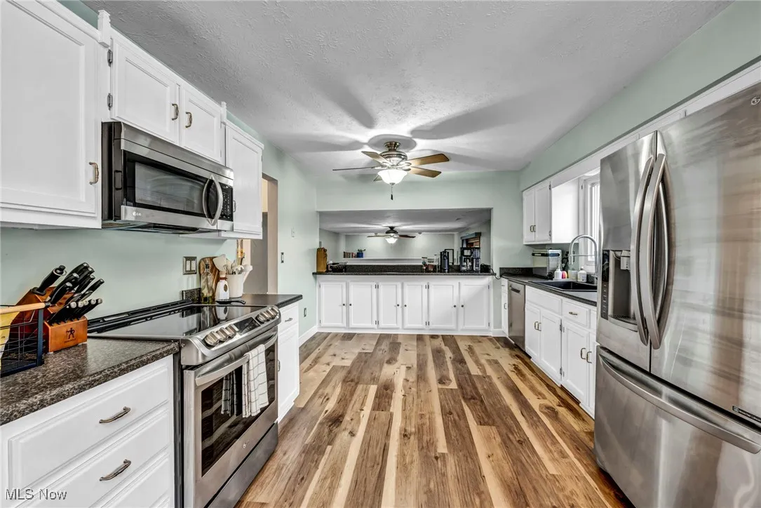 Kitchen featuring stainless steel appliances, white cabinetry, a ceiling fan, light wood-style flooring, and a textured ceiling